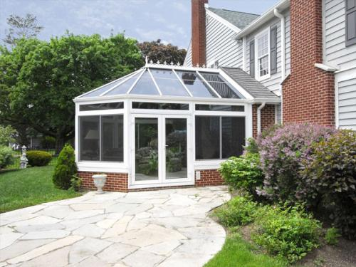 A conservatory pictured from outside that is attached to a brick home with a stone walkway leading up to it.
